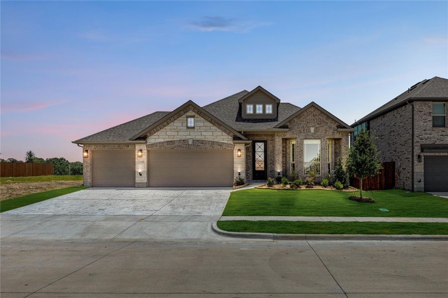Single-story brick and stone home with three-car garage, dormer window, and manicured front lawn at dusk