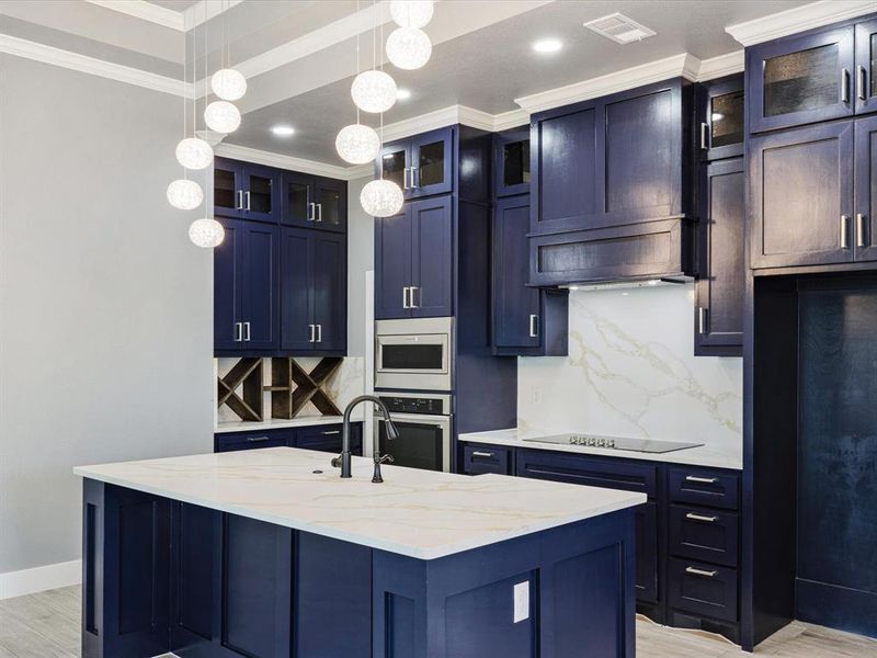 Kitchen with light stone counters, decorative backsplash, glass fronted cabinets, pendant lighting, and crown molding Kitchen with light stone counters, decorative backsplash, glass fronted cabinets, pendant lighting, and crown molding