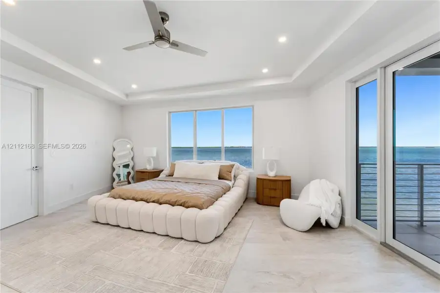 Tray ceiling with recessed lighting, large-format tile flooring, ceiling fan, and floor-to-ceiling glass sliding doors opening to an exterior balcony Tray ceiling with recessed lighting, large-format tile flooring, ceiling fan, and floor-to-ceiling glass sliding doors opening to an exterior balcony