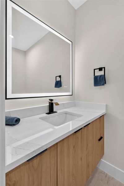 Sleek modern bathroom featuring a spacious vanity with a marble countertop, stylish wooden cabinetry, and an illuminated mirror for a touch of elegance.