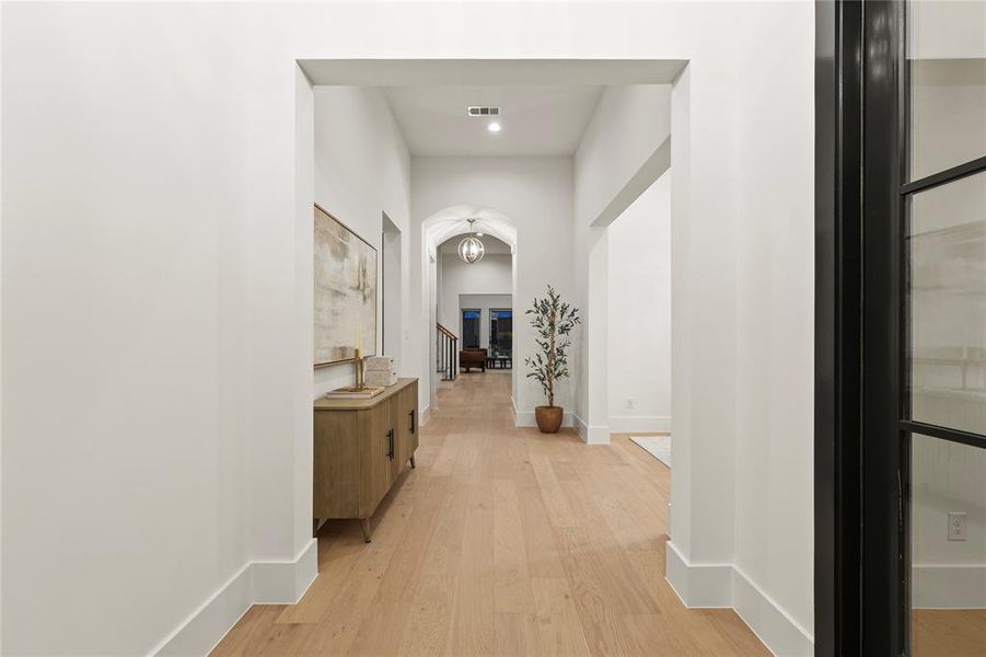 Corridor with light wood-style floors, arched walkways, stairs, and recessed lighting