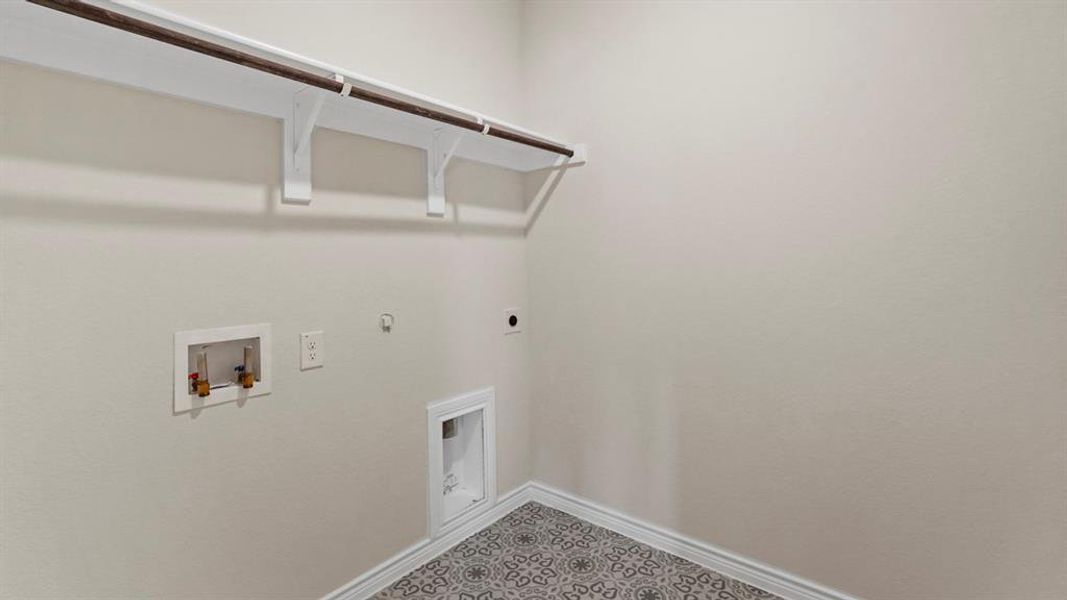 Laundry area featuring an overhead shelf with a clothing rod, patterned floor tiling, and neutral wall paint