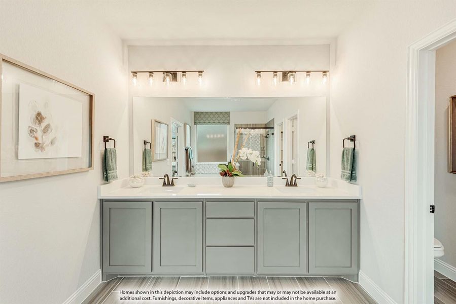 Bathroom with double vanity, gray cabinets, white countertops, and large mirror with overhead lighting
