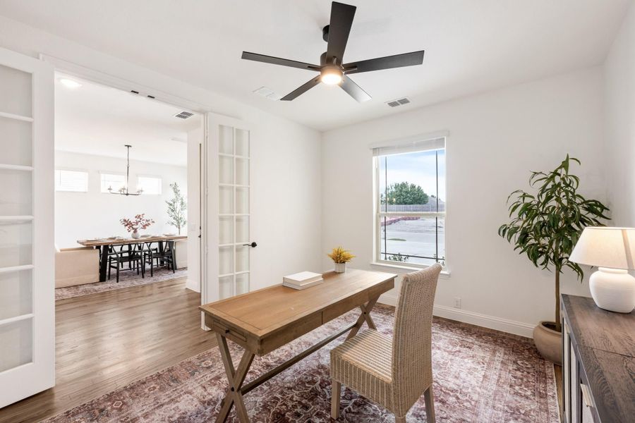 Home office with wood desk, wicker chair, ceiling fan, and French doors opening to dining room