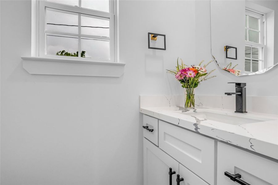 This elegant second bathroom exudes modern charm with its sleek white cabinetry, chic black accents, and a bright, airy feel enhanced by natural light from the window.