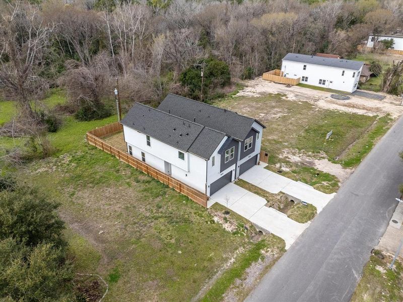 This aerial photo shows a newly constructed home with it's own separate driveways. The property has a fenced backyard and is situated on a spacious lot with surrounding greenery, offering privacy and room for outdoor activities.