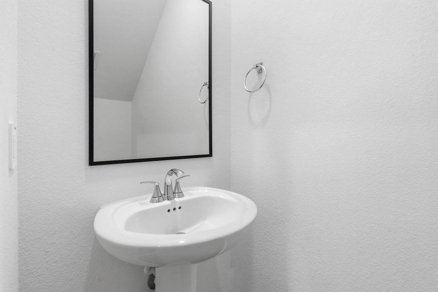 Pedestal sink with chrome faucet, complemented by a rectangular mirror with a black frame and a chrome towel ring Pedestal sink with chrome faucet, complemented by a rectangular mirror with a black frame and a chrome towel ring