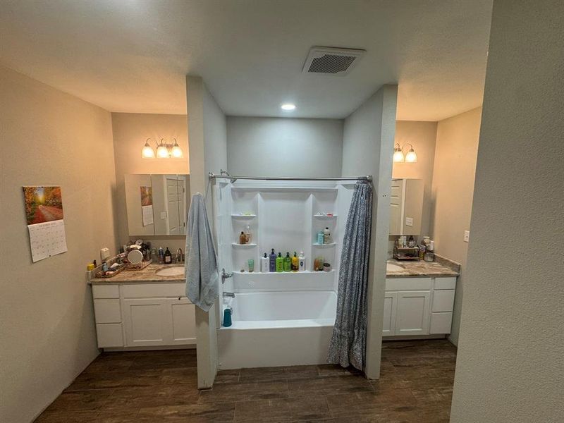 Bathroom featuring two vanities, dark wood-style floors, a textured wall, and shower / bath combo Bathroom featuring two vanities, dark wood-style floors, a textured wall, and shower / bath combo
