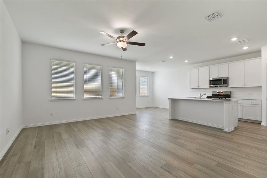 Kitchen featuring backsplash, appliances with stainless steel finishes, white cabinetry, and a center island with sink