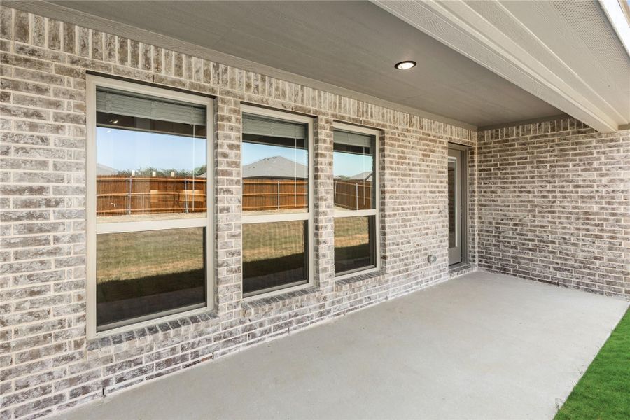 Covered back patio with concrete floor and three large windows on brick exterior wall Covered back patio with concrete floor and three large windows on brick exterior wall