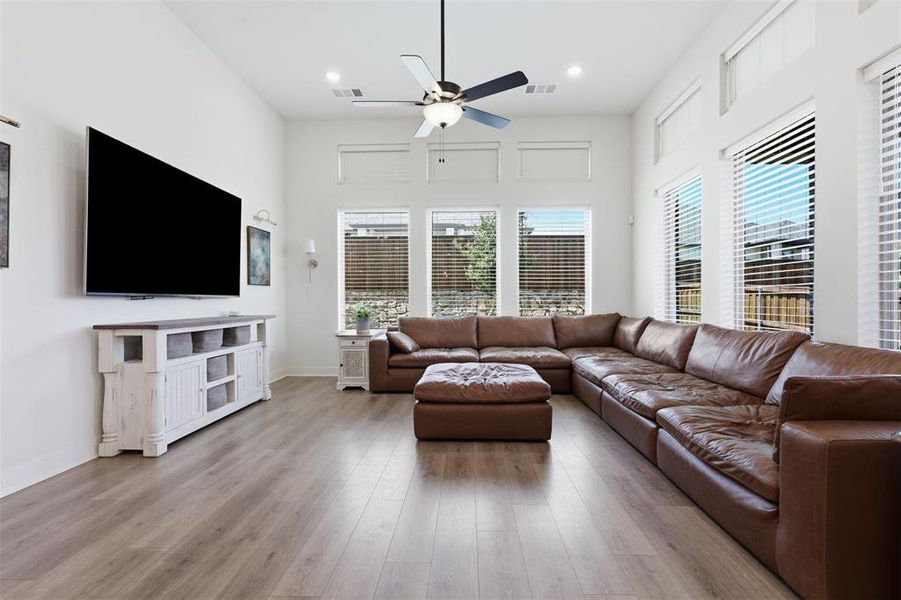 Spacious living area featuring high ceilings, wood-finish flooring, and ample natural light from multiple windows Spacious living area featuring high ceilings, wood-finish flooring, and ample natural light from multiple windows