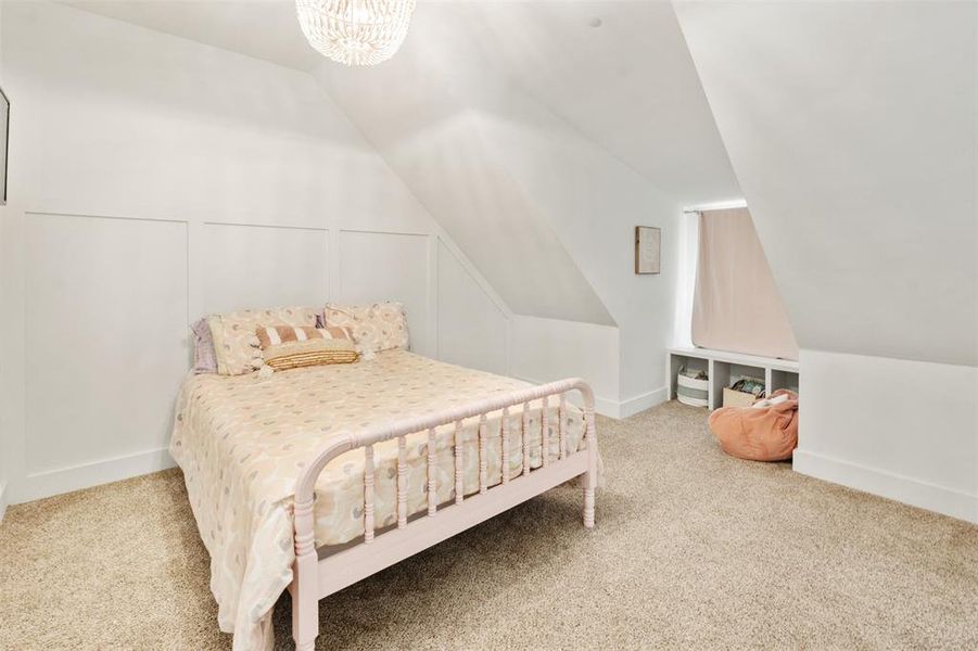 Bedroom with carpet, vaulted ceiling, a chandelier, and a decorative wall