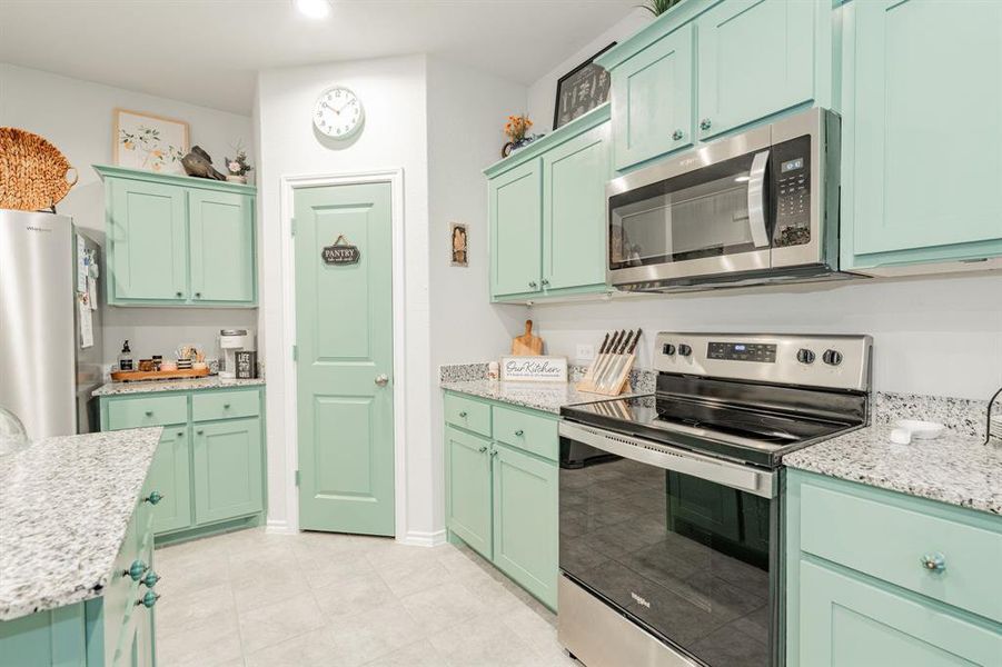 Kitchen with light stone counters, appliances with stainless steel finishes, and green cabinetry