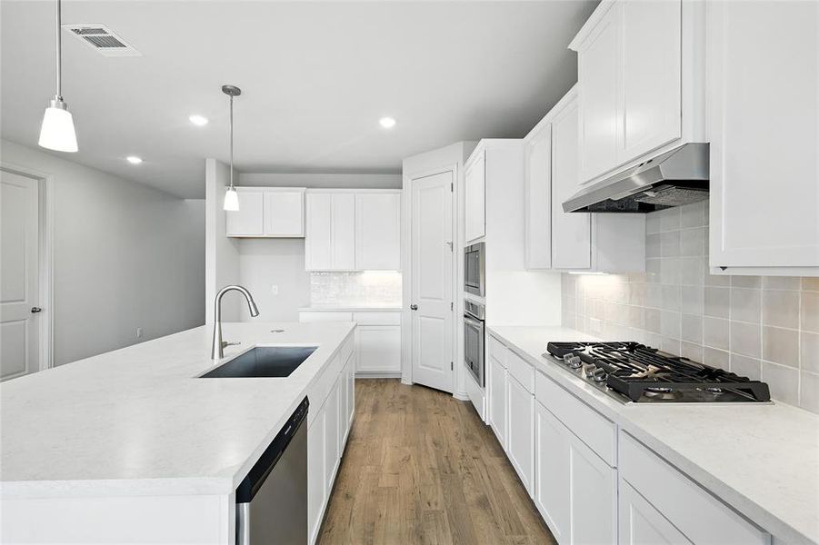 Kitchen with white cabinetry, a kitchen island with sink, wood finished floors, tasteful backsplash, and recessed lighting