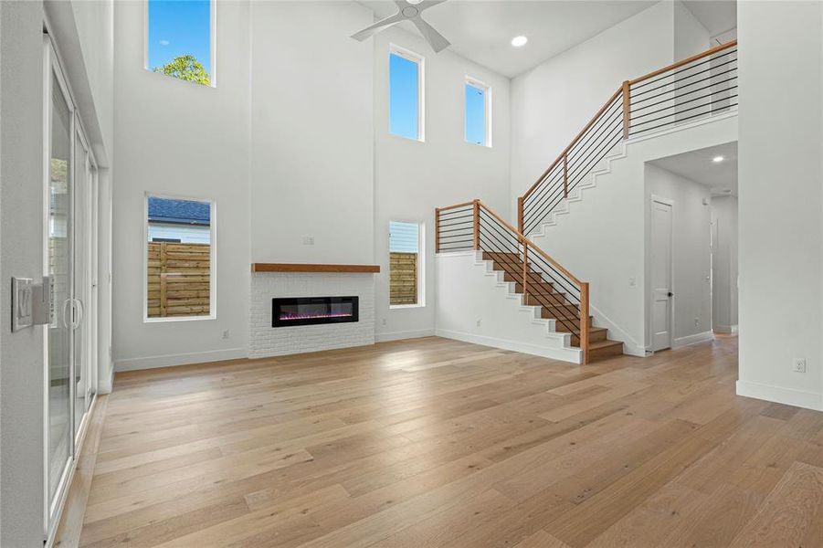 Unfurnished living room with a towering ceiling, light wood-style floors, stairway, plenty of natural light, and recessed lighting