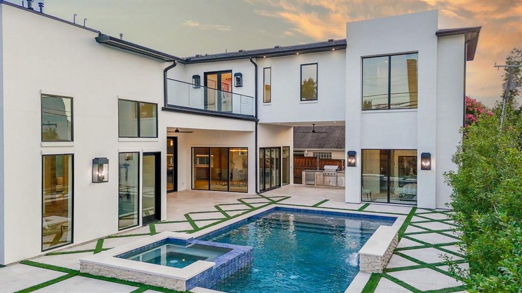 Back house at dusk featuring a patio area, a balcony, and a swimming pool with hot tub