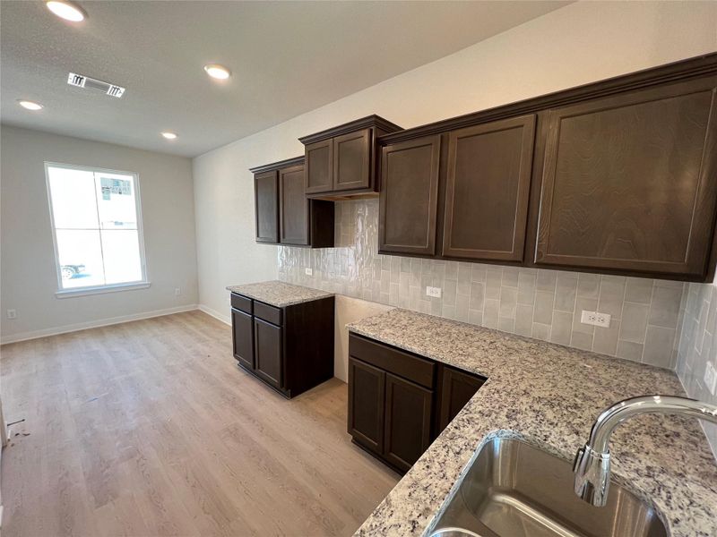 Kitchen featuring dark brown cabinetry, decorative backsplash, light stone countertops, light wood finished floors, and recessed lighting