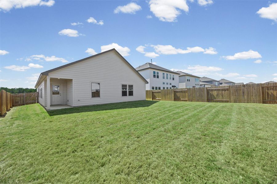 A spacious grassy lawn is fully enclosed by wooden fencing behind the home. A spacious grassy lawn is fully enclosed by wooden fencing behind the home.