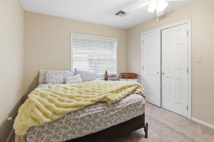 Neutral-toned bedroom featuring carpet flooring, a window with horizontal blinds, and a ceiling fan with integrated lighting