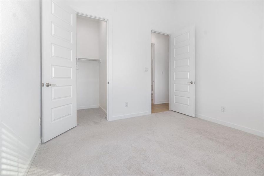 Unfurnished bedroom with light carpet and a walk in closet Unfurnished bedroom with light carpet and a walk in closet