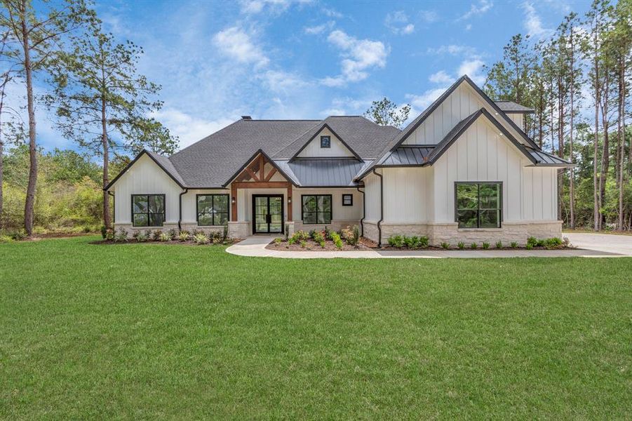 Modern 1.5 story home with a mix of stone and siding exterior, pitched roofs, and large windows. Surrounded by a lush green lawn and set against a backdrop of tall trees for privacy.