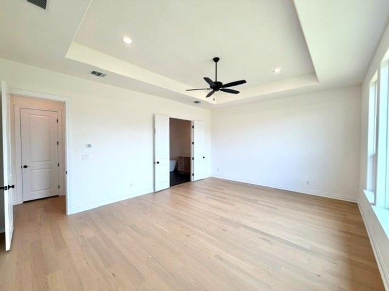 A spacious primary bedroom features beautiful hardwood flooring and a recessed ceiling with a contemporary ceiling fan. A spacious primary bedroom features beautiful hardwood flooring and a recessed ceiling with a contemporary ceiling fan.