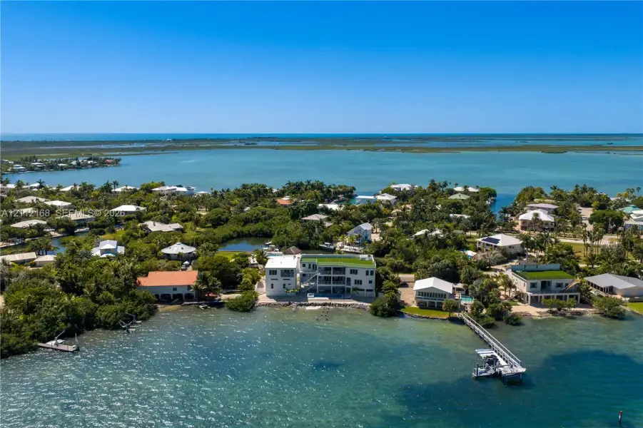 Waterfront estate featuring a multi-level structure with a flat roof, private dock, direct water access, and exterior balconies Waterfront estate featuring a multi-level structure with a flat roof, private dock, direct water access, and exterior balconies