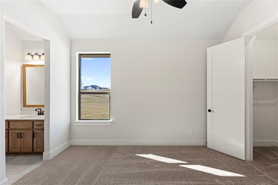 Unfurnished bedroom featuring sink, ensuite bath, ceiling fan, vaulted ceiling, and a walk in closet