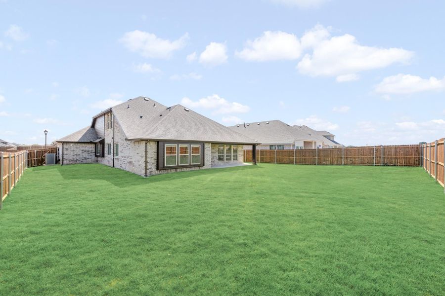 Backyard of brick home with large green lawn, covered patio, and wood privacy fence