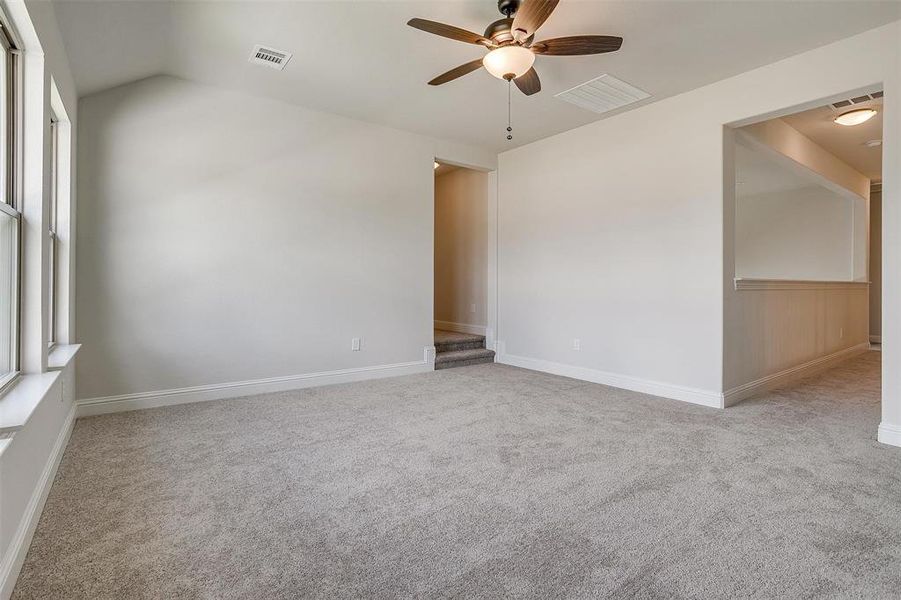 Empty room featuring light colored carpet, ceiling fan, and vaulted ceiling