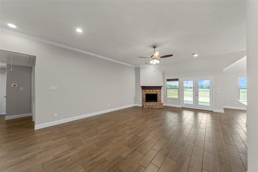 Spacious living area featuring wood-finish tile flooring, a brick fireplace with a wood mantle, and French doors