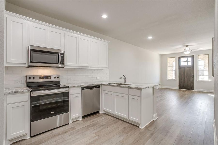 Kitchen featuring stainless steel appliances, white cabinets, light stone counters, a peninsula, and recessed lighting