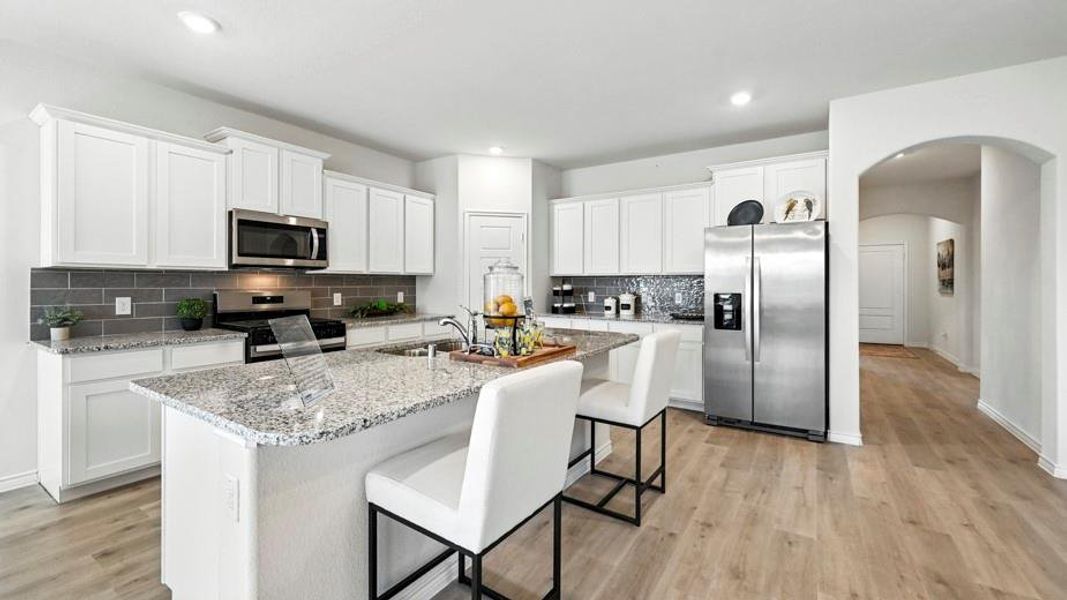 The kitchen features an island with a light-colored granite countertop, white cabinetry, stainless steel appliances, and light wood-style flooring