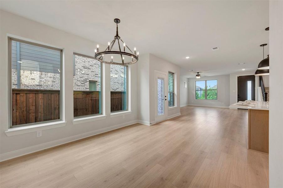 Expansive open-concept living area featuring light wood-finish flooring, a contemporary chandelier, multiple large windows, recessed lighting, and a kitchen island with pendant lighting