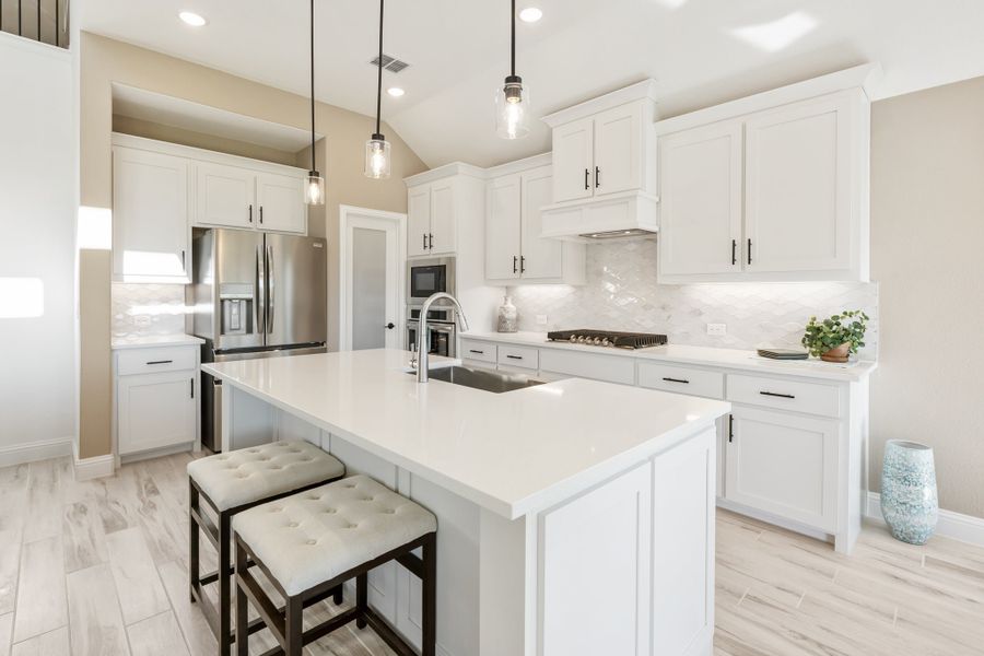 White kitchen with large island, pendant lights, stainless appliances, and two bar stools on light wood floors