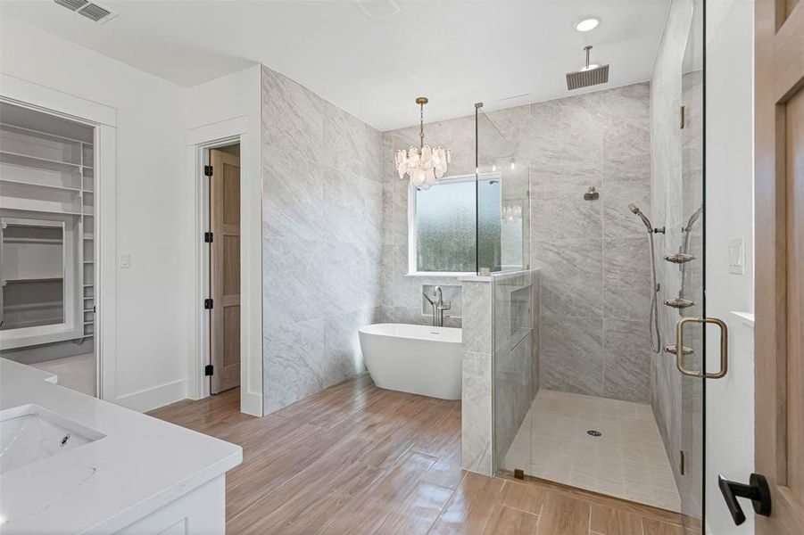 Bathroom featuring a marble finish shower, a soaking tub, double vanity, tile walls, and wood tiled floors Bathroom featuring a marble finish shower, a soaking tub, double vanity, tile walls, and wood tiled floors