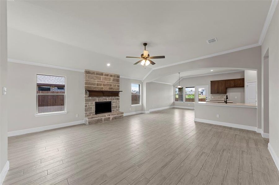 Unfurnished living room featuring ornamental molding, light wood-type flooring, a stone fireplace, vaulted ceiling, and ceiling fan
