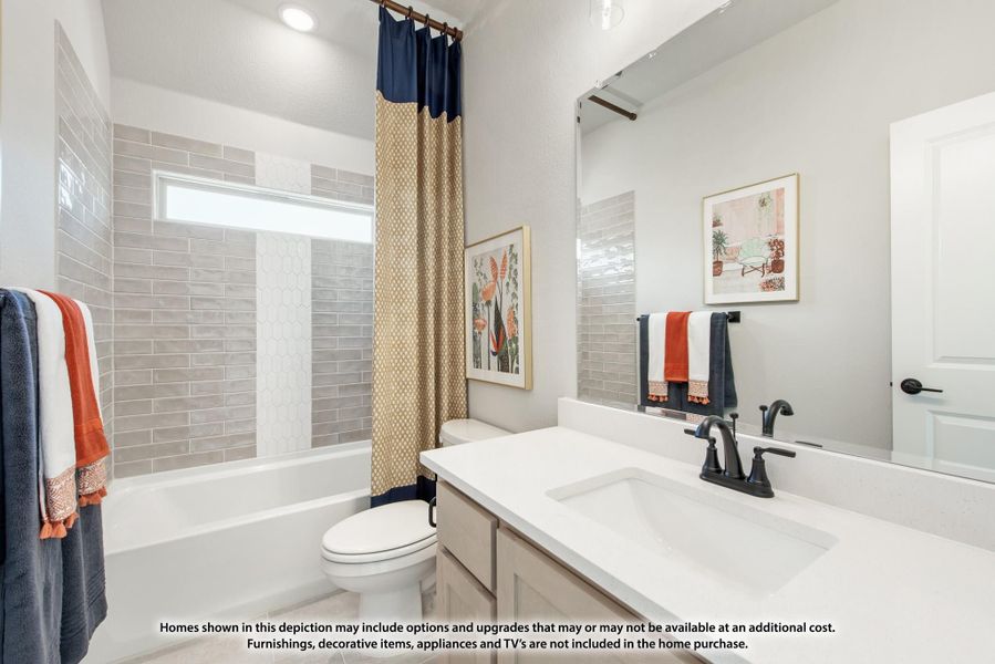 Bathroom with white vanity, gray tile tub surround, and patterned shower curtain over soaking tub