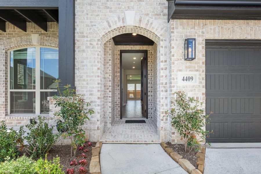 Brick home entrance with arched doorway, dark front door, house number 4409, and attached garage