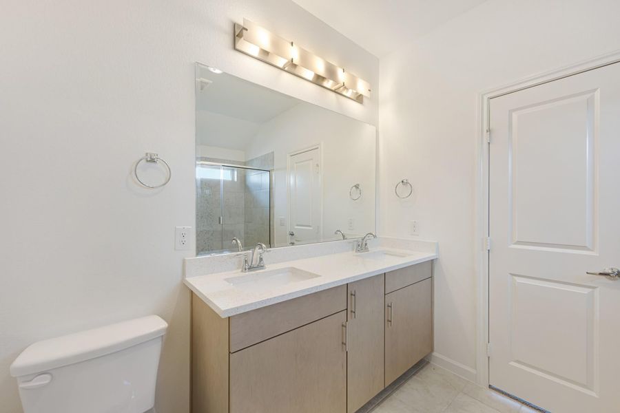 Bathroom with double sink vanity, wood cabinets, white countertop, large mirror, and glass shower visible in reflection. Bathroom with double sink vanity, wood cabinets, white countertop, large mirror, and glass shower visible in reflection.