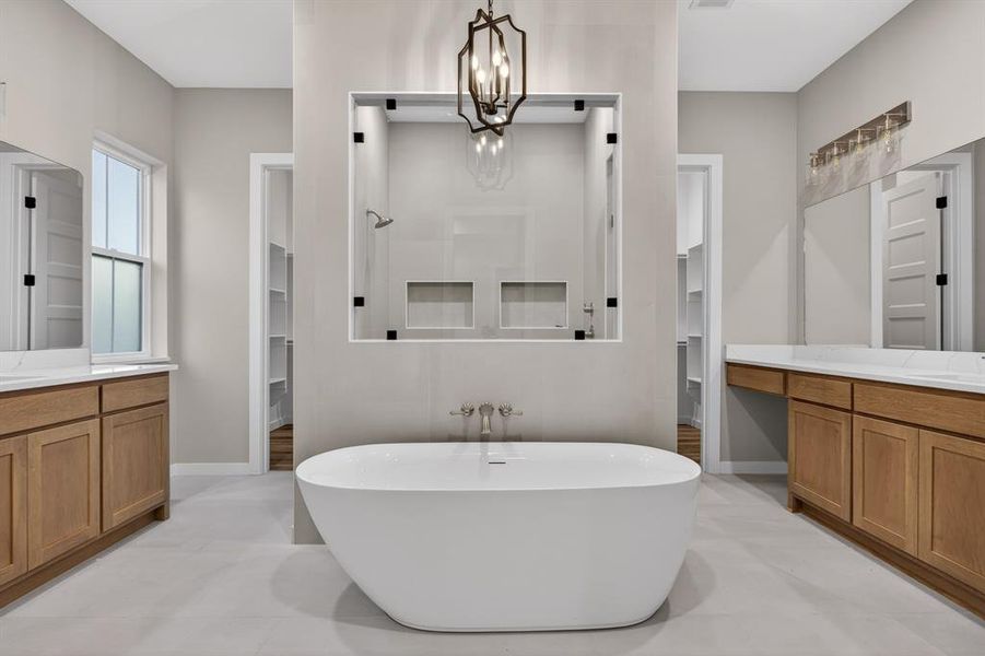 Oversized luxurious master bath features soaking tub, walk-in shower with custom tile work, glass doors, abundant cabinet storage, double vanities, and decorative lighting.