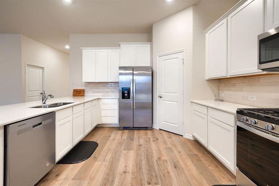 Kitchen featuring white cabinetry, appliances with stainless steel finishes, a peninsula, light wood-style floors, and light stone counters Kitchen featuring white cabinetry, appliances with stainless steel finishes, a peninsula, light wood-style floors, and light stone counters