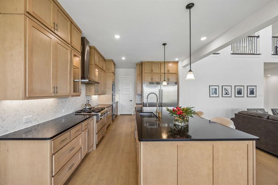 Kitchen with a spacious island, light wood-style floors, stainless steel appliances, hanging light fixtures, and dark stone counters