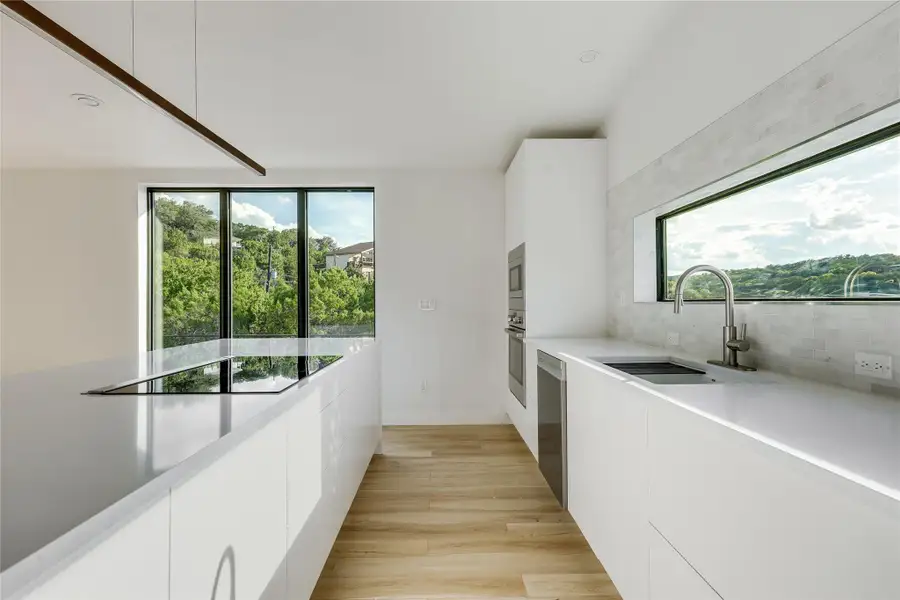 Kitchen featuring modern cabinets, white cabinetry, light wood-style floors, and decorative backsplash Kitchen featuring modern cabinets, white cabinetry, light wood-style floors, and decorative backsplash