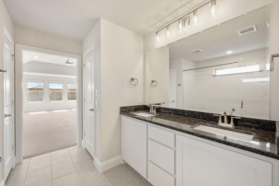Bathroom with double sink vanity, white cabinets, dark granite countertops, and large mirror with overhead lighting Bathroom with double sink vanity, white cabinets, dark granite countertops, and large mirror with overhead lighting