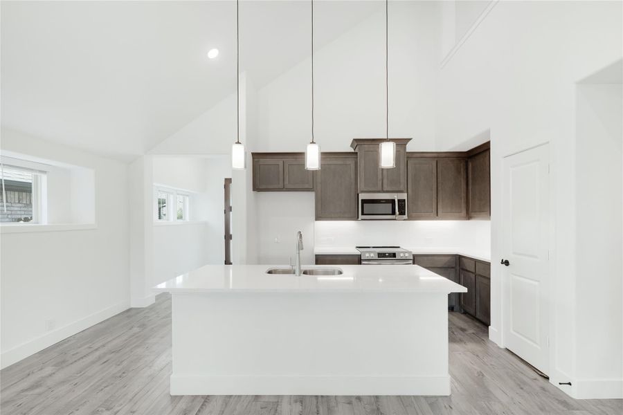 Kitchen with large white island, dark brown cabinets, stainless appliances, pendant lights, and vaulted ceiling Kitchen with large white island, dark brown cabinets, stainless appliances, pendant lights, and vaulted ceiling