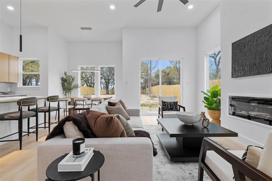 Living area with recessed lighting, healthy amount of natural light, a glass covered fireplace, ceiling fan, and a towering ceiling