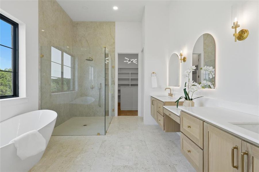 Contemporary bathroom featuring a freestanding soaking tub, a spacious glass-enclosed shower with tile surround, dual floating vanities with light wood-finish cabinetry, and arched illuminated mirrors