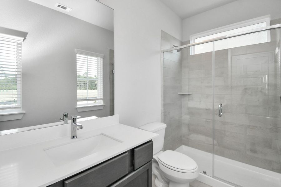 Secondary bath features tile flooring, a walk-in shower with tile surround, light stained wood cabinets, beautiful light countertop. Secondary bath features tile flooring, a walk-in shower with tile surround, light stained wood cabinets, beautiful light countertop.