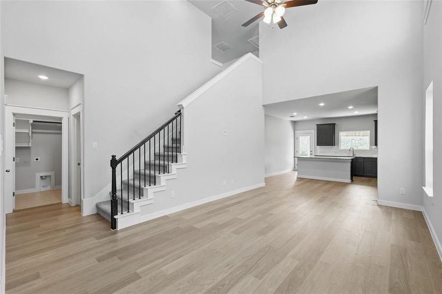 Unfurnished living room featuring a high ceiling, stairs, a ceiling fan, light wood-style floors, and a sink